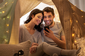 Image showing happy couple with smartphone in kids tent at home