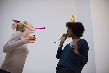 Image showing smiling women in party caps blowing to whistles