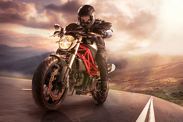 Image showing biker on mountain highway, riding around a curve with a motion b