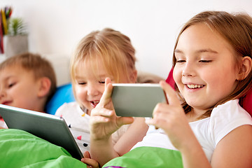 Image showing happy kids with tablet pc and and smartphone in bed 