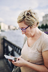 Image showing Aged woman browsing smartphone on embankment