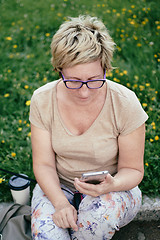 Image showing Elderly woman in casual outfit, sitting on the grass in the park