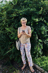 Image showing Senior woman using smartphone near bush