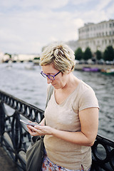 Image showing Aged woman browsing smartphone on embankment