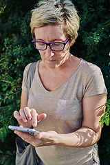 Image showing Senior woman using smartphone near bush