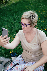 Image showing Elderly woman in casual outfit, sitting on the grass in the park