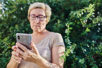 Image showing Senior woman using smartphone near bush