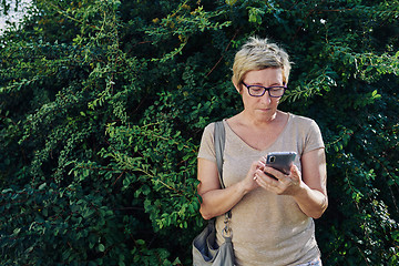 Image showing Senior woman using smartphone near bush