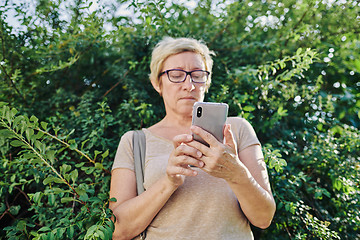 Image showing Senior woman using smartphone near bush