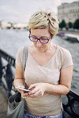 Image showing Aged woman browsing smartphone on embankment