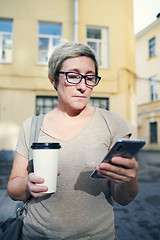 Image showing Senior woman with drink using smartphone