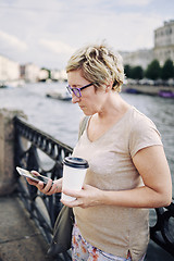 Image showing Aged woman browsing smartphone on embankment