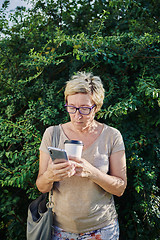 Image showing Senior woman using smartphone near bush