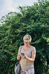 Image showing Senior woman using smartphone near bush