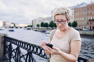 Image showing Aged woman browsing smartphone on embankment