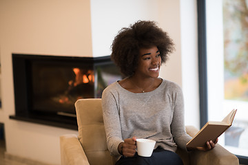 Image showing black woman reading book  in front of fireplace