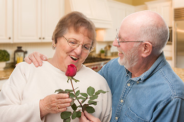 Image showing Happy Senior Adult Man Giving Red Rose to His Wife Inside Kitche