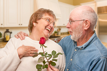 Image showing Happy Senior Adult Man Giving Red Rose to His Wife Inside Kitche