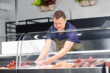 Image showing male seller with seafood at fish shop fridge