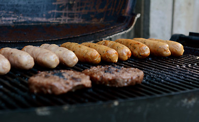 Image showing Beefburgers and sausages cooking on an open grill