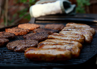 Image showing Rows of sausages and hamburgers on a barbecue