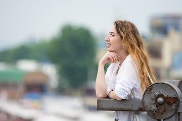 Image showing A young girl looks into the distance leaning on the old fence