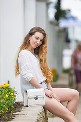 Image showing A young girl with a lady\'s white handbag crouched on the parapet and looked at the frame