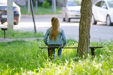 Image showing A teenage girl is sitting on a bench near a tree in the courtyard of the house