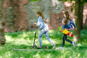 Image showing The girl is riding happily on the scooter, behind her runs another girl with a skate in her hands