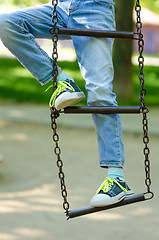 Image showing Legs of a child in sneakers with light green laces on a metal ladder on chains