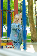 Image showing The girl joyfully and fervently laughs sitting on a hanging ladder in the playground