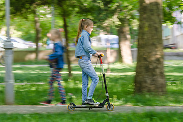 Image showing The girl is happily riding a scooter along an asphalt road