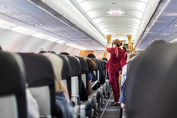 Image showing Stewardess in red uniform giving safety instructions on commercial passengers airplane.