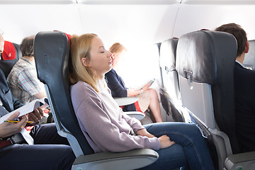 Image showing Tired blonde casual caucasian lady napping on seat while traveling by airplane. Commercial transportation by planes.