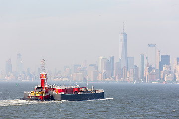 Image showing Freight tug pushing cargo ship to the port in New York City and Lower Manhattan skyscarpers skyline in background.