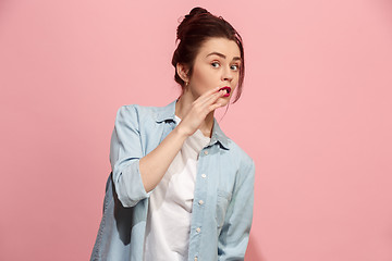 Image showing The young woman whispering a secret behind her hand over pink background