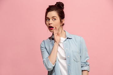 Image showing The young woman whispering a secret behind her hand over pink background