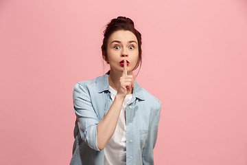 Image showing The young woman whispering a secret behind her hand over pink background