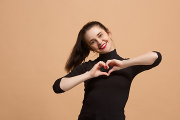 Image showing Portrait of attractive cute girl with bright makeup smiling with a heart isolated over pastel background