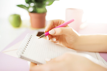 Image showing The female hands holding pen. The phone on trendy pink desk.