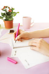 Image showing The female hands holding pen. The phone on trendy pink desk.