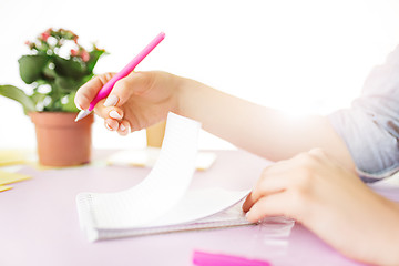 Image showing The female hands holding pen. The phone on trendy pink desk.