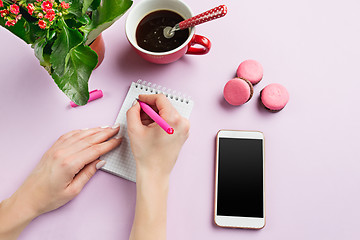 Image showing The female hands holding pen. The phone and french macarons on trendy pink desk.