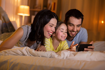 Image showing happy family with smartphone in bed at night