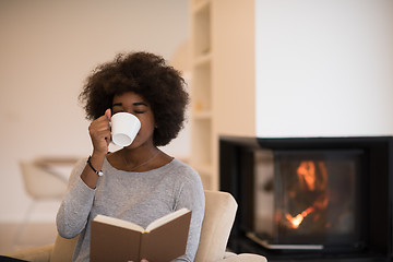 Image showing black woman reading book  in front of fireplace