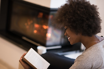 Image showing black woman reading book  in front of fireplace