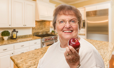 Image showing Happy Senior Adult Woman with Red Apple Inside Kitchen.