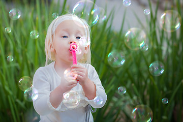 Image showing Adorable Little Girl Sitting On Bench Having Fun With Blowing Bu