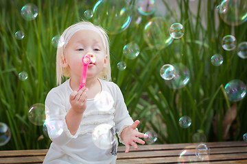 Image showing Adorable Little Girl Sitting On Bench Having Fun With Blowing Bu