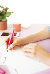 Image showing The female hands holding pen. The phone on trendy pink desk.